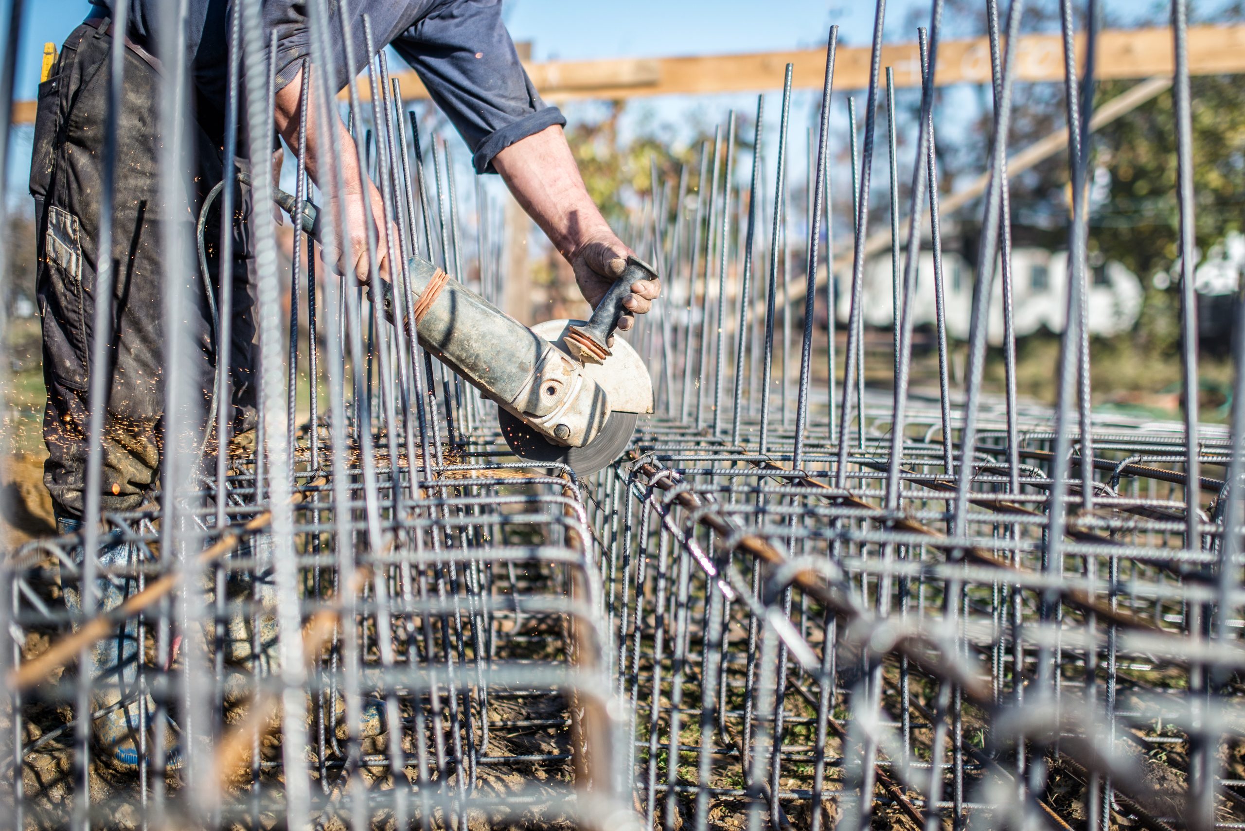 Worker using an angle grinder to cut steel bars used for reinforcement at construction site